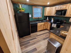 A kitchen with wooden cabinets, a black refrigerator, a microwave, and a stove. - *Pet Friendly* Peaceful 3 bd w hot tub, fire pit, games (Sevierville)