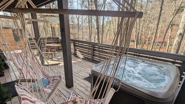 Een houten terras met een jacuzzi, een hangmat en een houten omheining.
