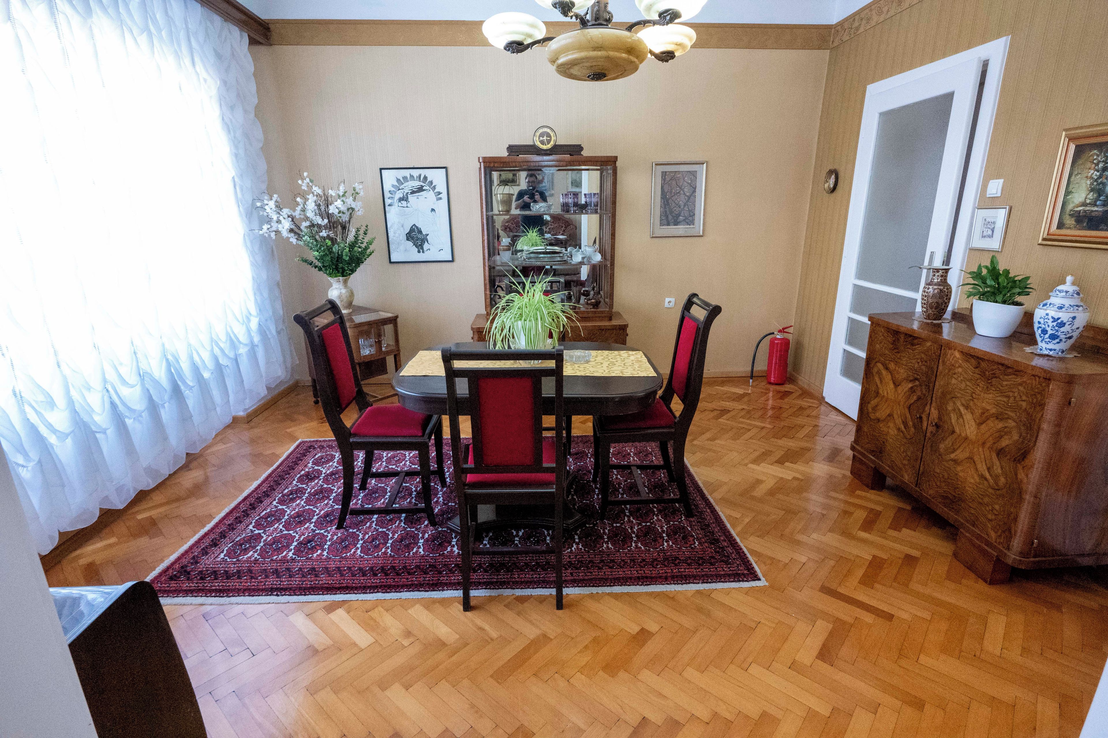 Un espace repas avec une table en bois, des chaises rouges, un lustre et un tapis rouge.