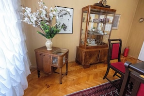 A room with a wooden cabinet, a glass display case, a vase with flowers, and a chair. - Vijecnica Grand Apartment Sarajevo - Free Garage Parking (Sarajevo)
