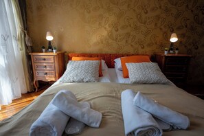 A neatly made bed with rolled towels, two bedside tables with lamps, and a floral wallpaper pattern. - Vijecnica Grand Apartment Sarajevo - Free Garage Parking (Sarajevo)