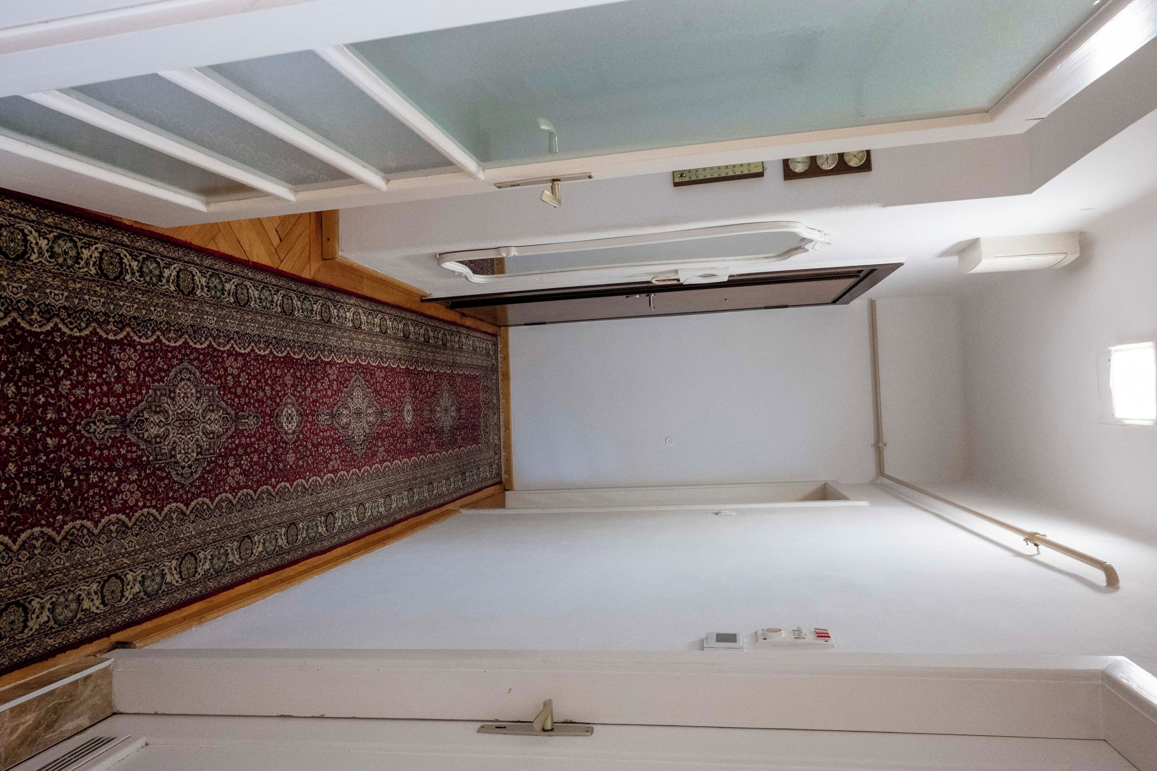 Una habitación con tragaluz, alfombra estampada y pared blanca con un ventanal pequeño.