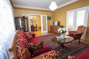 A living room with a sofa set, a coffee table, and a patterned rug. There is a television on a wooden cabinet and a door leading to another room. - Vijecnica Grand Apartment Sarajevo - Free Garage Parking (Sarajevo)