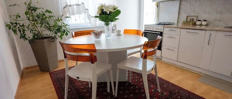 Un comedor con una mesa redonda, cuatro sillas, una planta en maceta y un florero con flores.