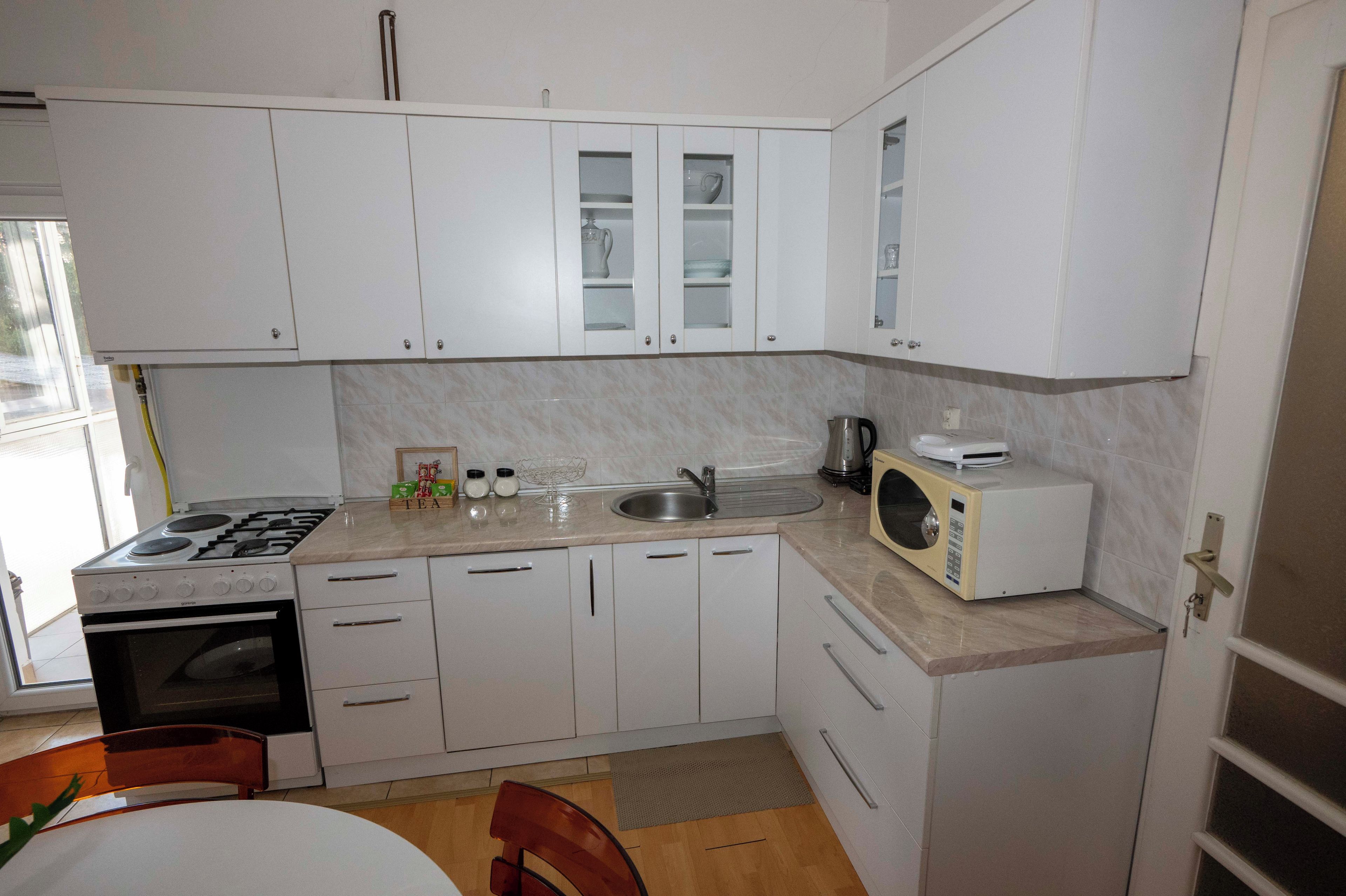 Una cocina pequeña con gabinetes blancos, estufa, microondas y lavamanos.