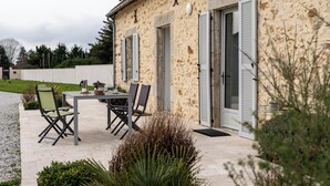 An outdoor patio with a table and chairs, surrounded by plants and a stone wall. - La Closerie blanche - 5km Le Mans - Wifi (Yvré-l'Évêque)
