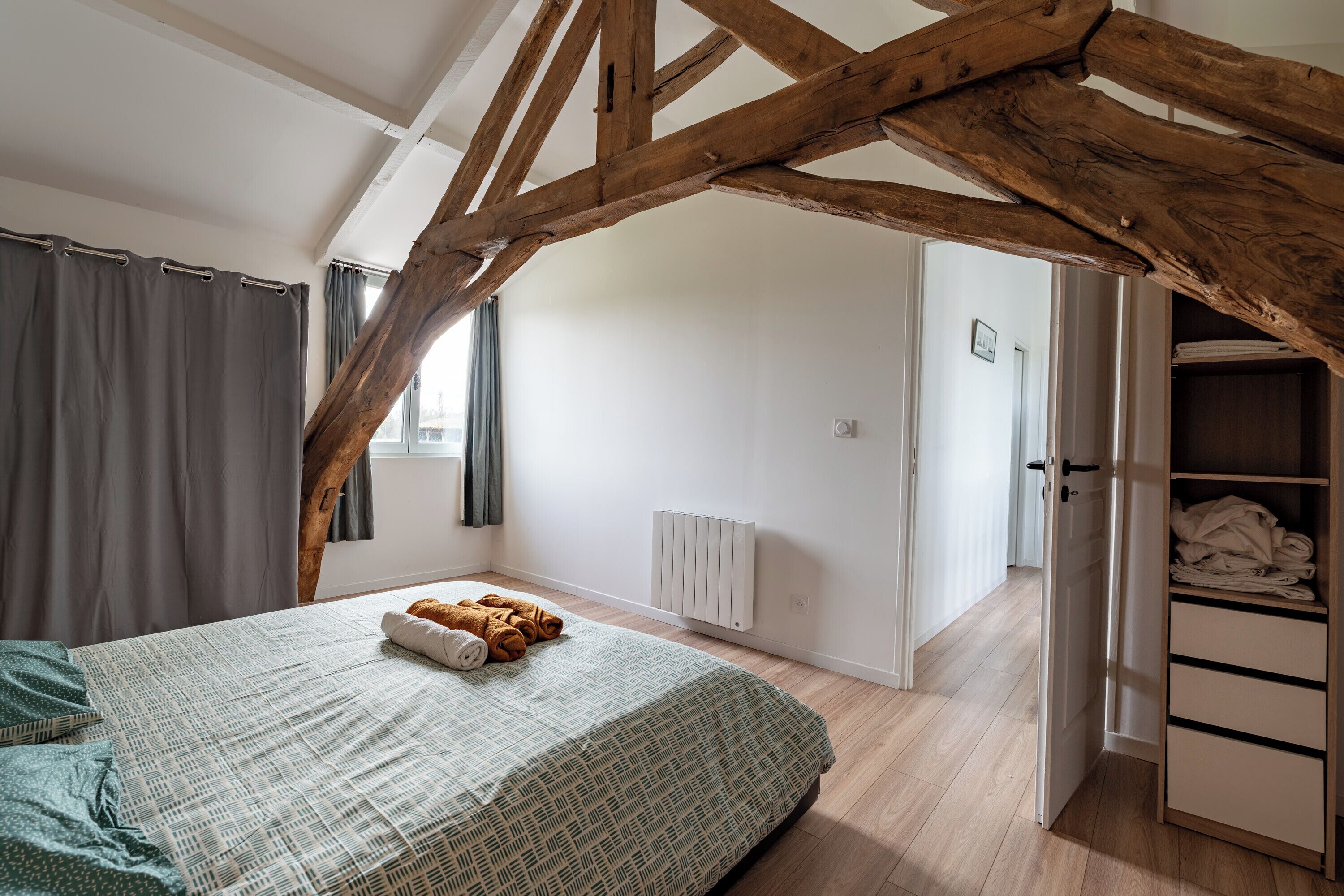 A bedroom with a sloped ceiling, a bed with a patterned bedspread, a radiator, and a wardrobe.