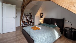 A bedroom with a sloped ceiling, a bed with patterned bedding, a bedside table with a lamp, a bookshelf, and a door. - La Closerie blanche - 5km Le Mans - Wifi (Yvré-l'Évêque)