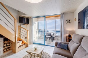 A modern living room with a sofa, a coffee table, a TV mounted on the wall, and a staircase with a wine rack. - Panorama Marin - Parking - Mer (Bretignolles-sur-Mer)