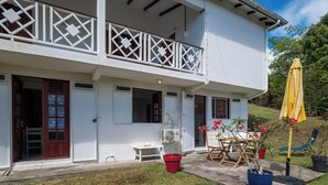A two-story building with a balcony, a small outdoor seating area, and potted plants. - L’écrin - Climatisation - Jardin (Baillif)