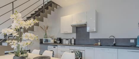 Une cuisine moderne avec des meubles blancs, un four encastré et un coin repas comprenant une table et des chaises.