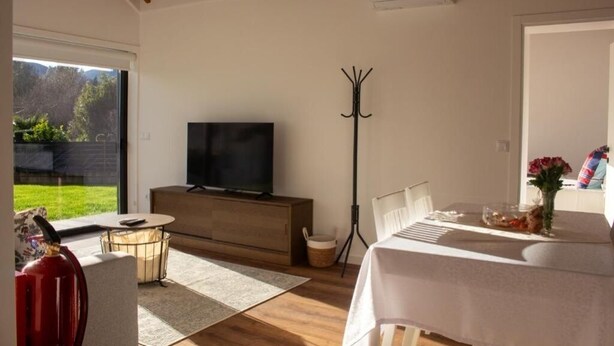 A modern living room with a flat-screen TV, a dining table, and a large window offering a view of the outdoors. - CasadoZé - Ihr privates Ferienhaus mit Pool und Gartenblick in Arcos de Valdevez (Arcos de Valdevez)