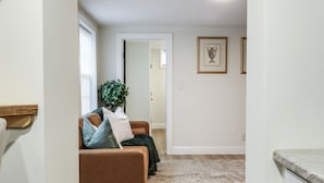 A hallway with a brown leather sofa, a green plant, and a white rug. - Walkable 1BR in Village of Horseheads, Near I-86, Corning & Finger Lakes (Horseheads)