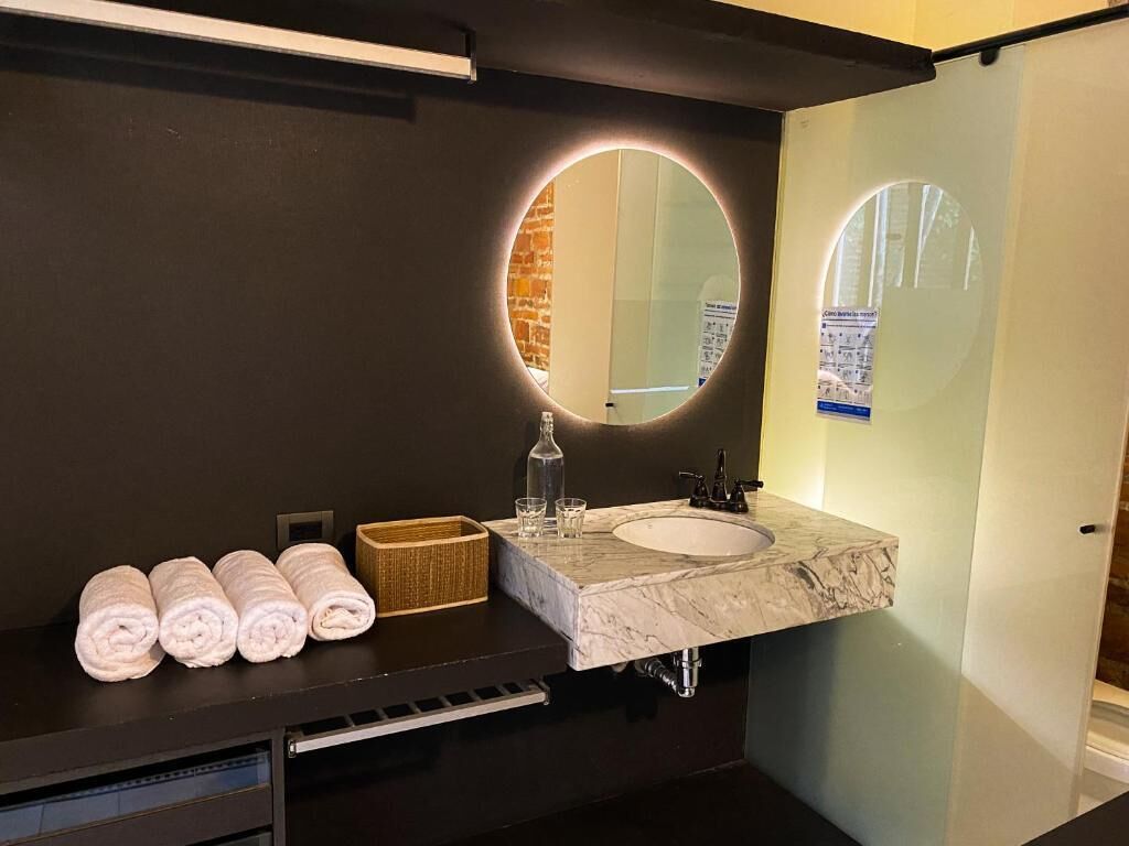 A modern bathroom with a marble sink, a round mirror, and neatly rolled towels on the counter.