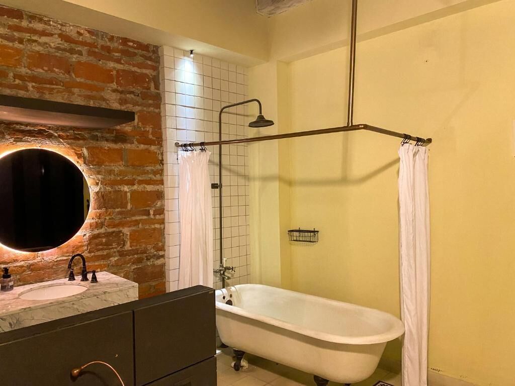 A bathroom with a vintage bathtub, a round mirror, and a brick wall.