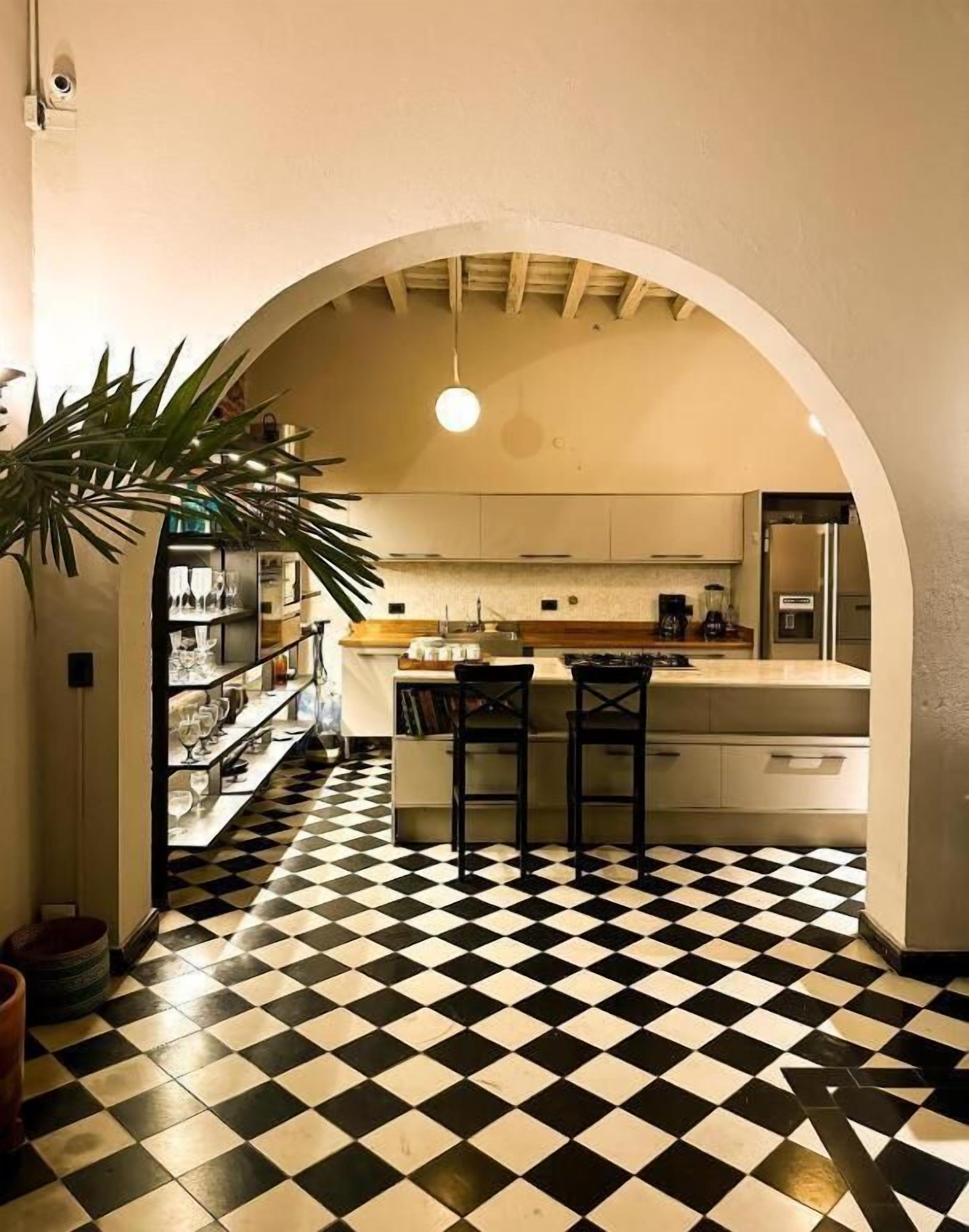 A kitchen with a checkered floor, an archway, and a bar area with stools.