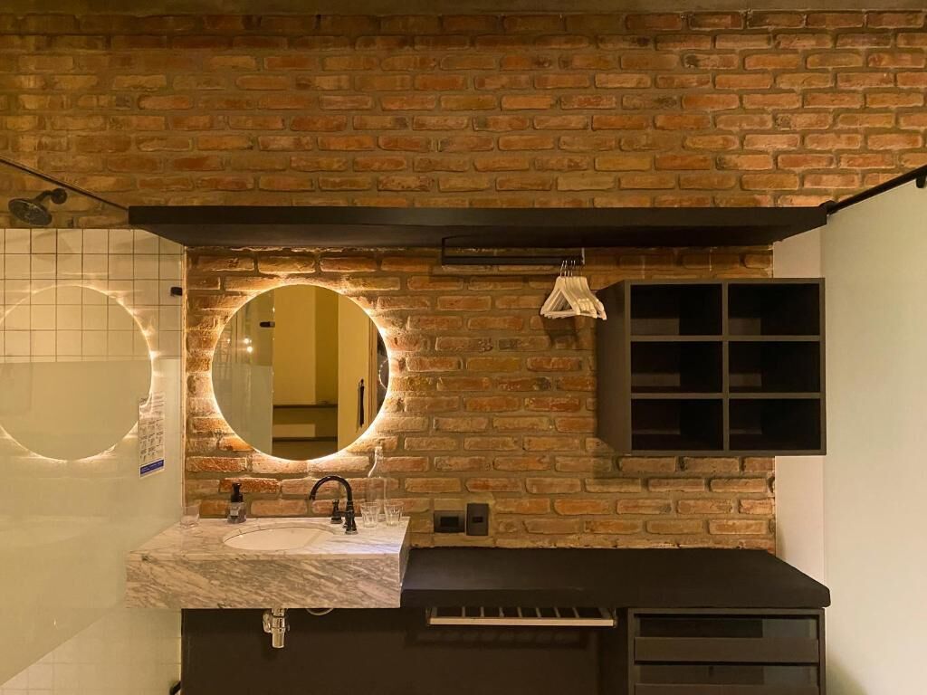 Ein Badezimmer mit Backsteinwand, einem runden Spiegel mit Beleuchtung, einem Waschbecken und einem Handtuchhalter.