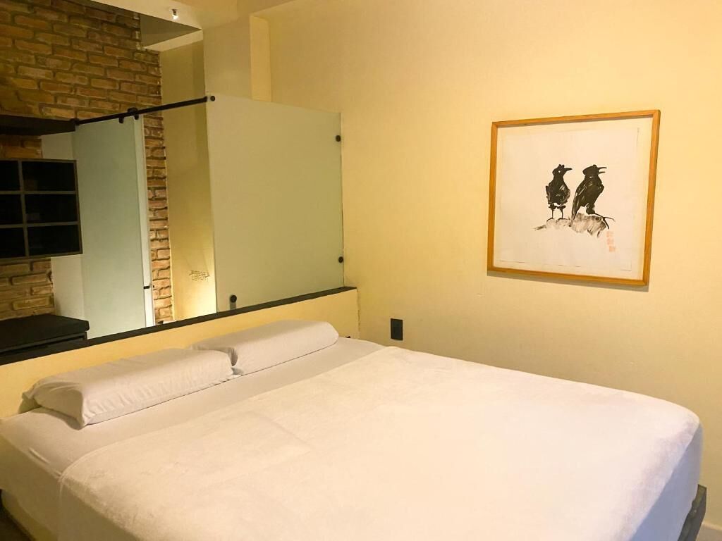 Una habitación de hotel con una cama, un espejo, una obra de arte enmarco de aves y una pared de ladrillo.