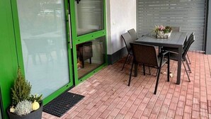 Une terrasse avec une table et des chaises, une porte verte et une plante en pot.