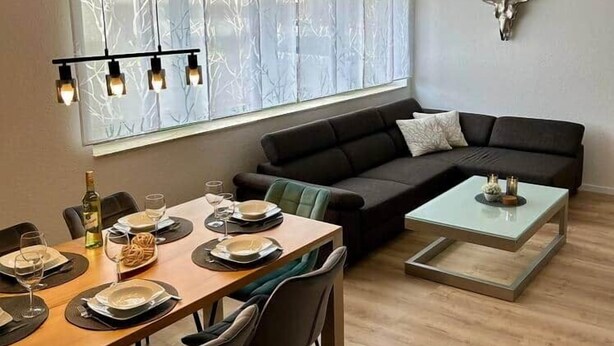Un salon moderne comprenant un coin repas, un canapé noir, une table basse en verre et une décoration murale représentant une tête de taureau.