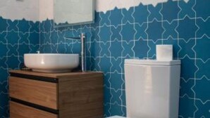 Ein Badezimmer mit einer weißen Toilette, einem hölzernen Waschtisch mit einer weißen Spüle und einer blauen, mit einem geometrischen Muster versehenen Wand.