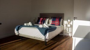 Ein Zimmer mit einem Einzelbett, Holzboden, weißen Wänden und einem Kopfstück mit Karomuster.