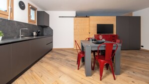 Una cucina moderna con un piano di lavoro scuro, un forno integrato e un’area pranzo in legno con un tavolo grigio e sedie rosse.