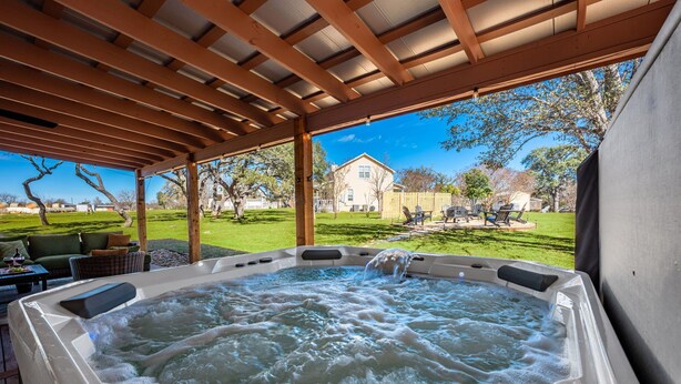 Ein Whirlpool unter einer Holzpergola mit Blick auf ein Haus und Garten.