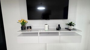 A modern living room with a large flat-screen TV mounted on a white wall, a white entertainment unit below, and a tiled floor.