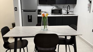 A modern kitchen with a white marble countertop, black cabinets, a stainless steel refrigerator, a black microwave, and a black sink. There is a vase with flowers on the countertop.