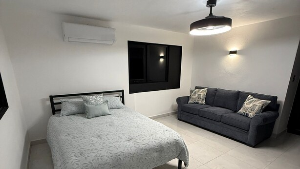 A bedroom with a bed, a sofa, a wall-mounted TV, and a ceiling light.