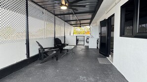 An outdoor covered area with a metal roof, a seating area with benches and a table, and a view of a building with a door and windows.