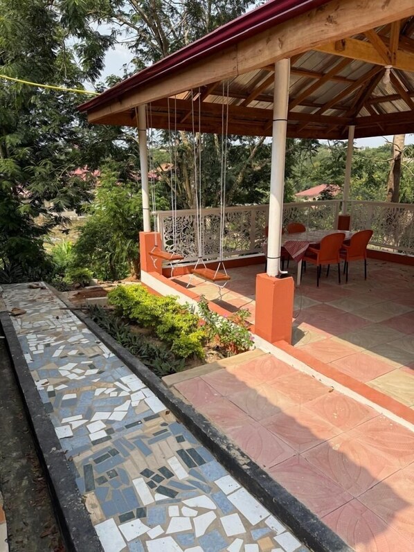 Un patio techado al aire libre con un columpio, un sendero de baldosas y una zona de estar con sillas.