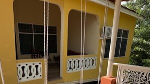 Un edificio amarillo con un porche cubierto, un columpio y una barandilla decorativa.