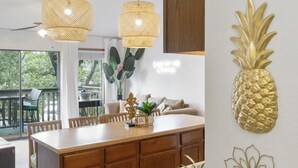 Una cucina moderna con mobili in legno, un'isola centrale, luci a sospensione e decorazioni murali tra cui un'ananas e un fiore.