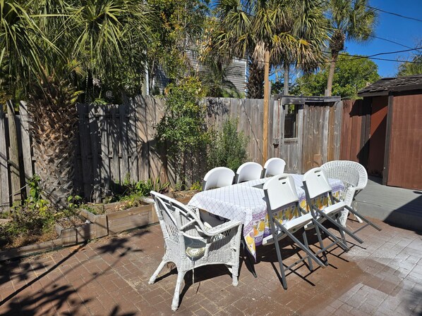 Une terrasse avec une table et des chaises, entourée d’une clôture en bois et de palmiers.