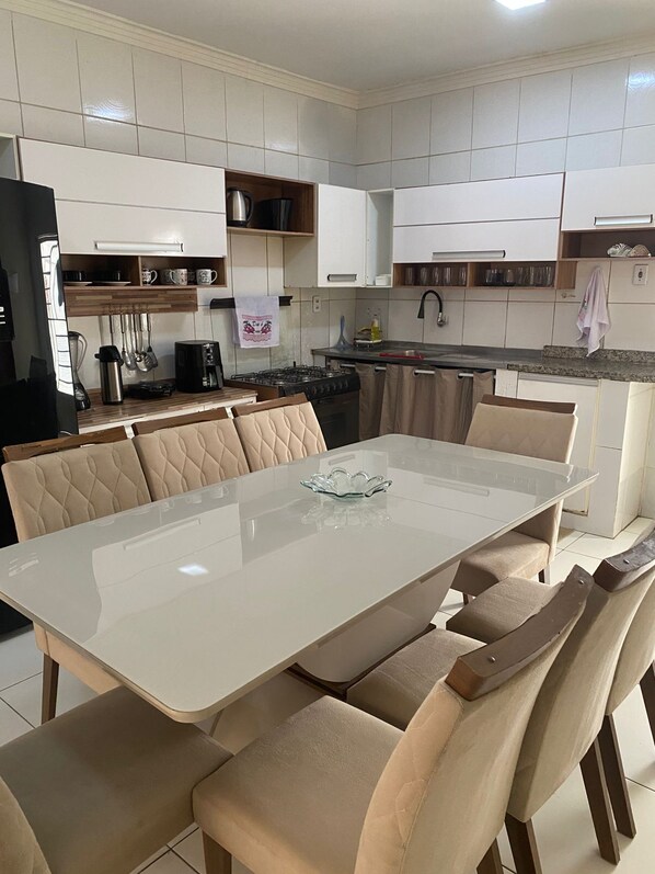 A modern kitchen with white cabinets, a dining table with beige upholstered chairs, and a stainless steel coffee maker.