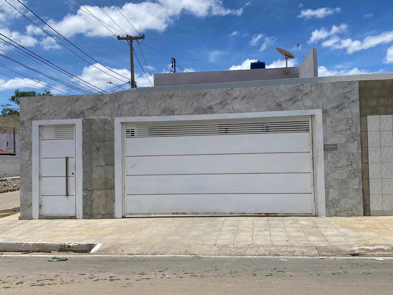 Um edifício moderno com uma grande porta de garagem, antena parabólica no telhado e calçada pavimentada.
