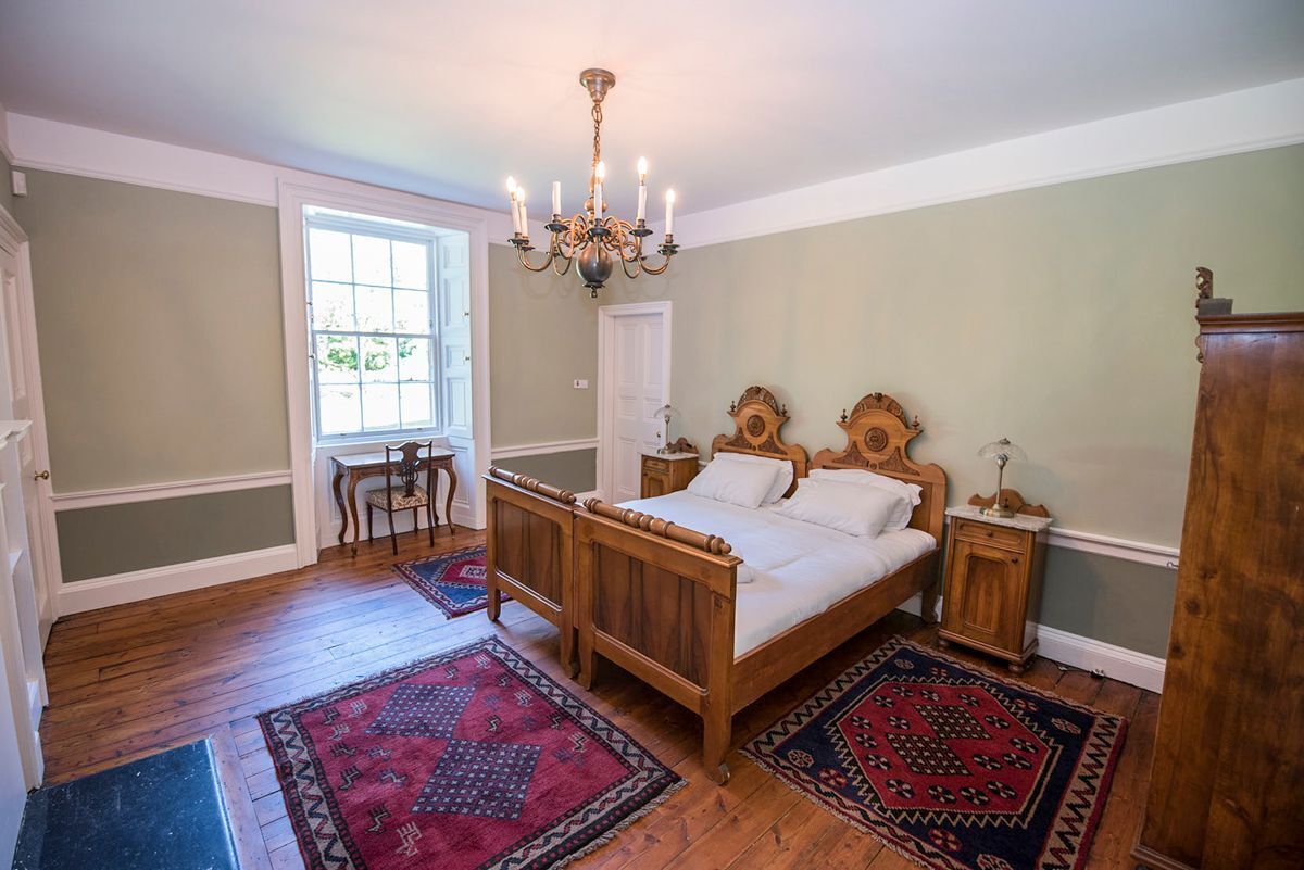 Une chambre à coucher avec un lit en bois, un lustre, une fenêtre et une porte.