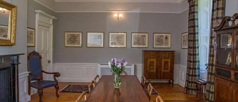 Een formele eetzaal met een grote houten tafel, een gedetailleerd schitterend kroonluchter en klassieke decoratie.