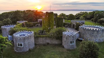 Un château doté de nombreuses tours et entouré de douves, avec une végétation luxuriante et une étendue d’eau en arrière-plan.