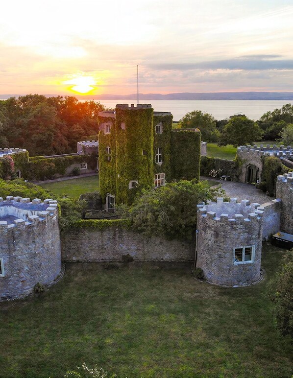 A castle with a tower covered in ivy, surrounded by stone walls and a moat.