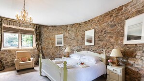 Un dormitorio con pared de piedra, una cama, una silla y un ventanal con cortinas.