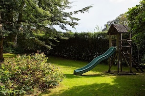 Ein Spielplatz mit Rutsche und Holzspielhaus.
