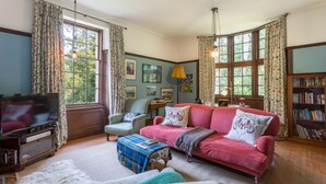 Ein gemütliches Wohnzimmer mit Fernseher, einem roten Sofa, einem blauen Sessel und einem Bücherregal.