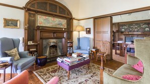 Ein traditionell eingerichtetes Wohnzimmer mit Kamin, blauem Sessel, Sofa und Couchtisch mit Büchern.