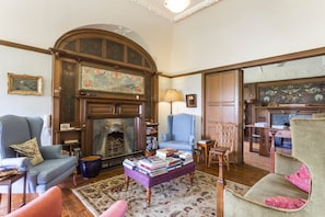 Ein traditionell eingerichtetes Wohnzimmer mit Kamin, blauem Sessel, Sofa und Couchtisch mit Büchern.
