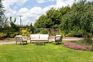 A garden with a stone wall, a wooden bench, and a white sofa with two chairs. - Emley Woodhouse - Seven Bedroom Villa, Sleeps 17 (Emley)