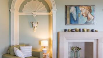 Un salon avec un canapé vert, une lampe blanche, une cheminée et un tableau accroché au mur.
