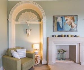 A living room with a green sofa, a white lamp, a fireplace, and a painting on the wall. - Emley Woodhouse - Seven Bedroom Villa, Sleeps 17 (Emley)